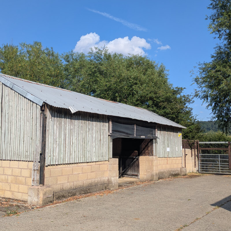 Picture of a barn that is only has one entrance that is opened, the barn has greyish panelling on its side panel and roof